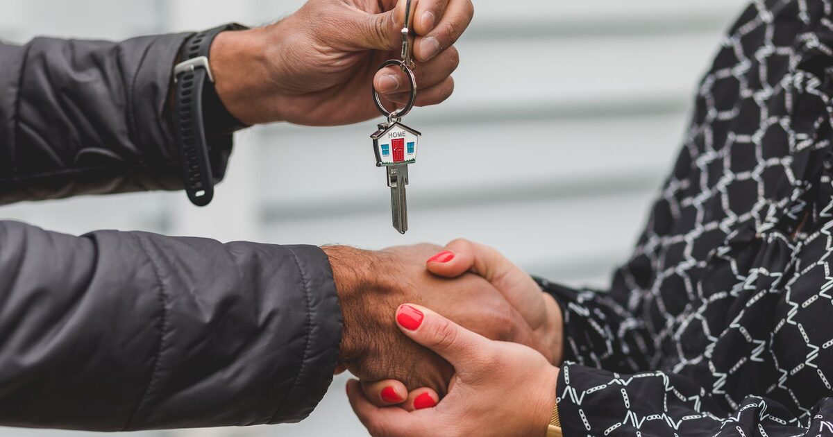 A real estate agent handing over house keys and shaking hands with a client outside a home